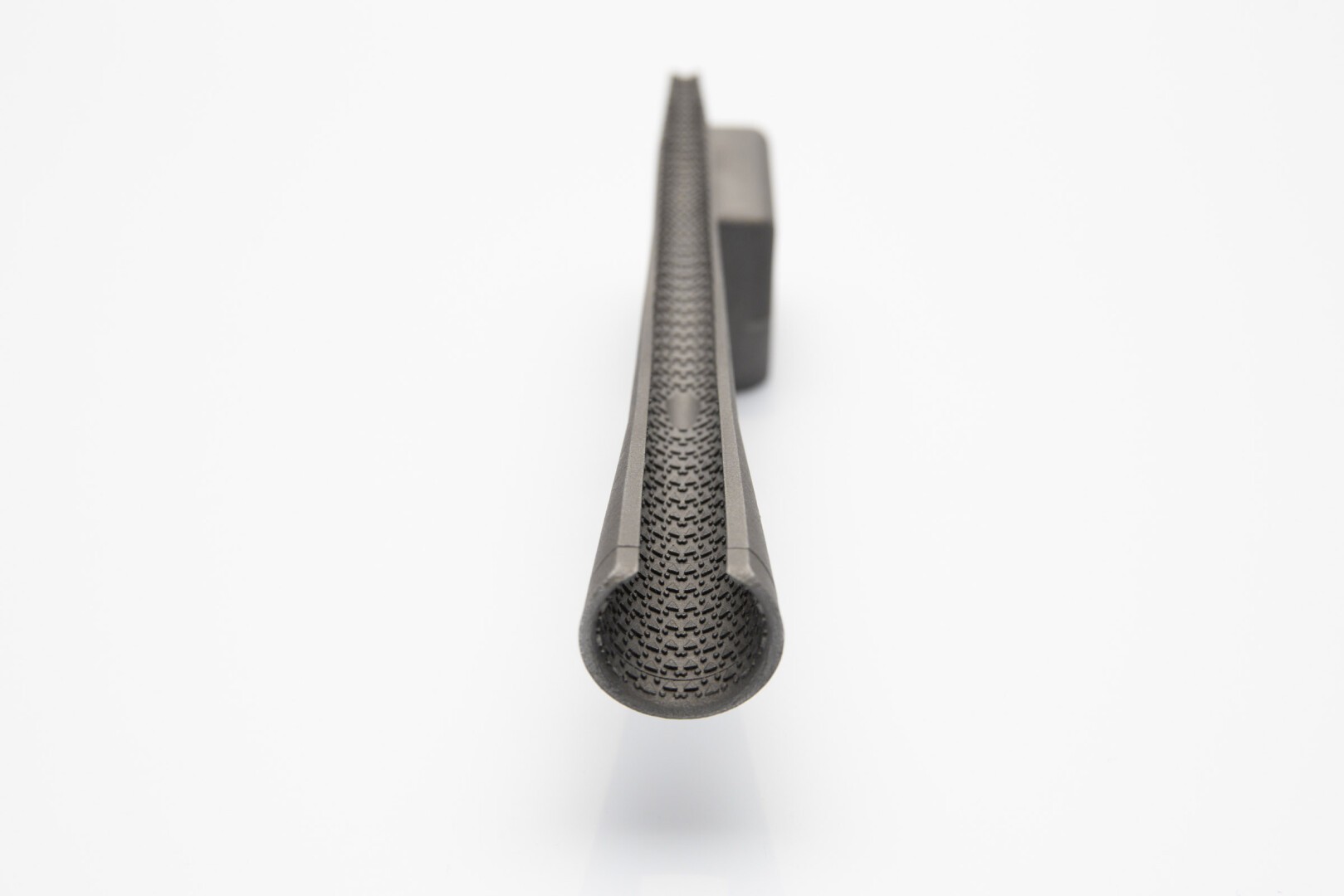 Close-up of a black, cylindrical object made of carbon fiber with a hollow core, viewed from the front against a white background. The woven texture of the material is clearly visible.