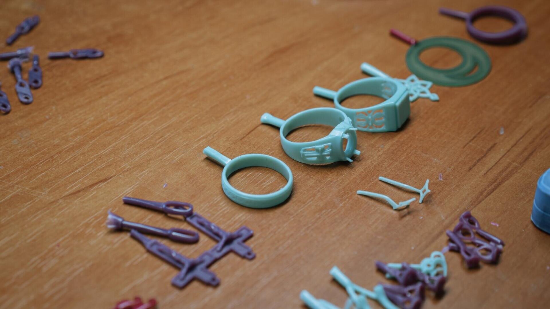 Plastic molds for rings and other jewelry parts in teal and purple are scattered on a wooden surface. Some molds are circular, while others are shaped for earrings or pendants.