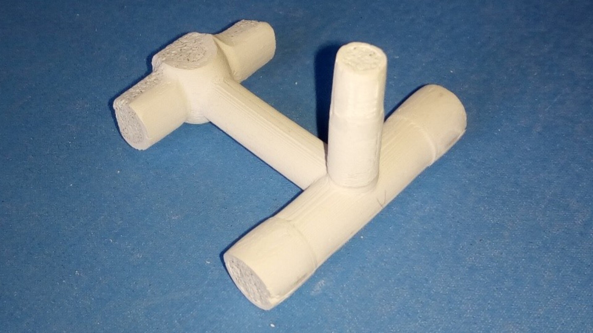White cylindrical chalk sticks arranged on a blue surface to form a T-shape, with one stick standing vertically and others lying horizontally, intersecting at right angles.