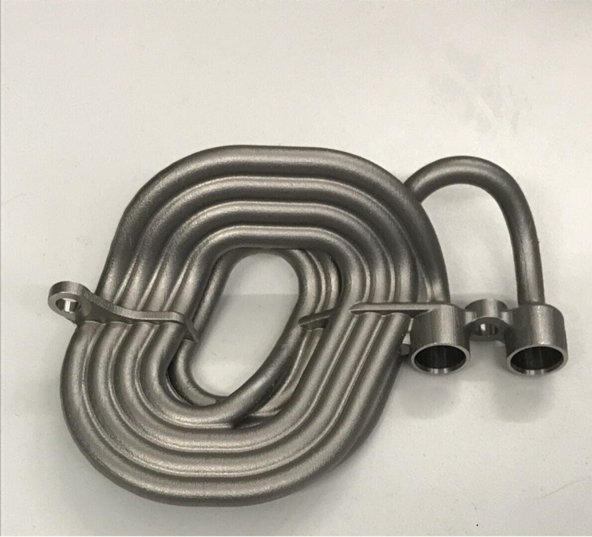 Ein metallisches Spiralrohr mit zwei offenen zylindrischen Enden und Montagehalterungen, platziert auf einer schlichten weißen Oberfläche. Das Rohr scheint Teil einer mechanischen oder industriellen Komponente zu sein.