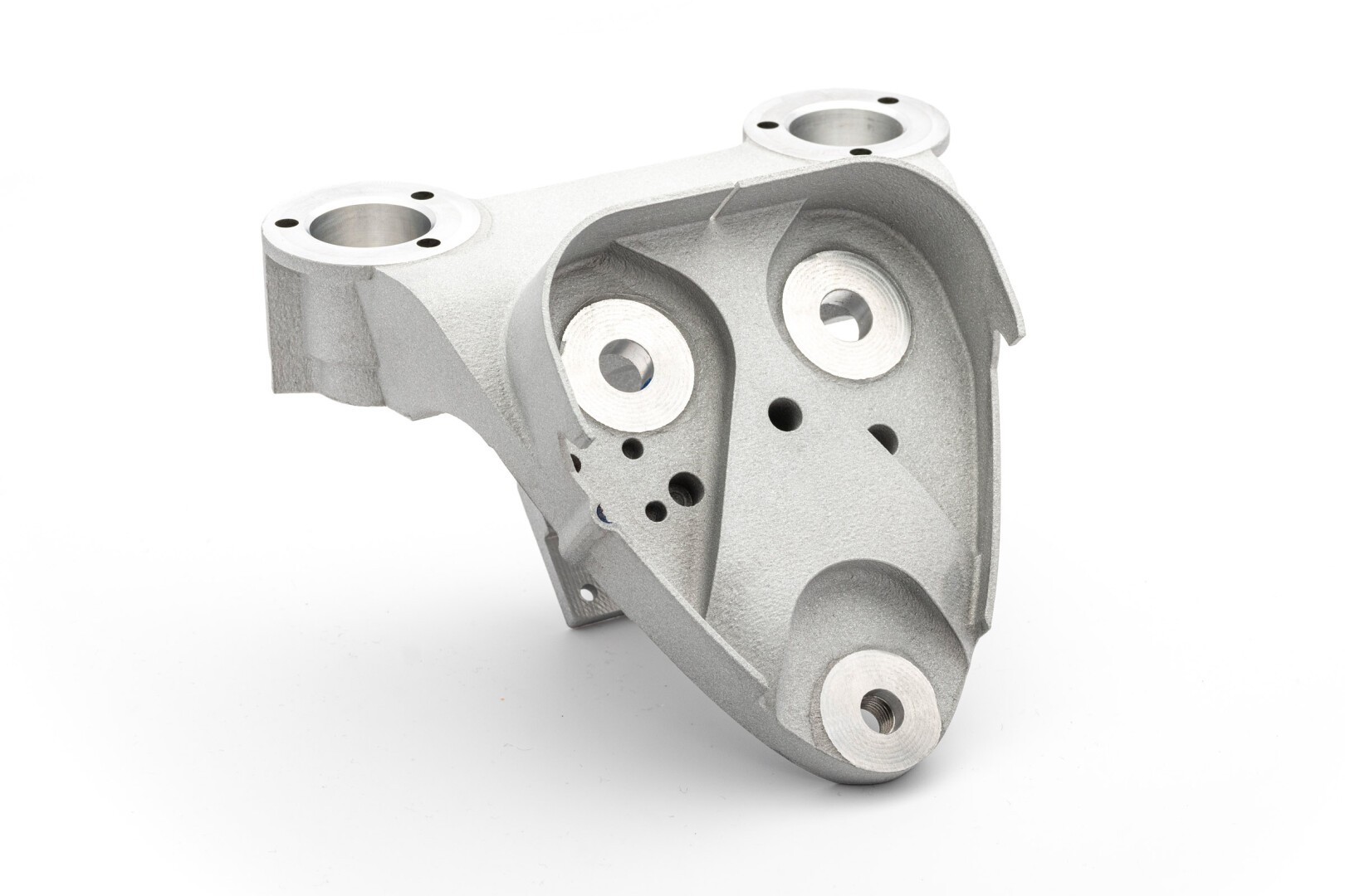 A machined metal component with a complex geometric shape, multiple circular openings, and a textured, matte silver-grey surface, photographed on a white background.