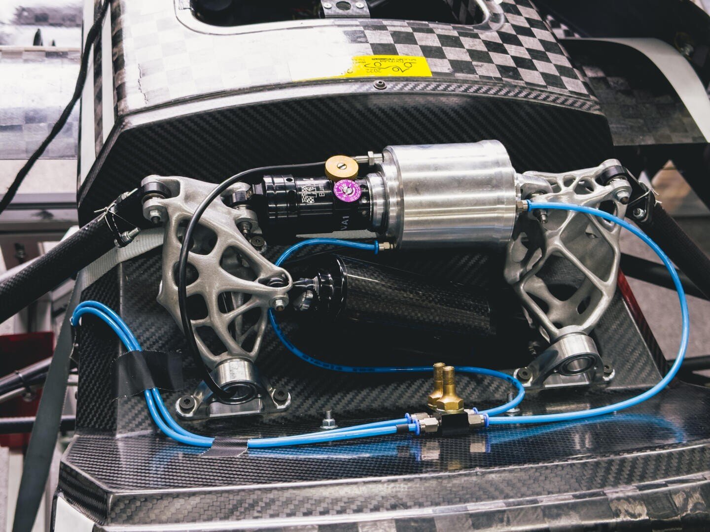 Nahaufnahme eines Rennwagen-Aufhängungssystems mit freiliegenden Metallkomponenten, blauer Verkabelung und Kohlefaserelementen, die die komplizierten technischen und mechanischen Details hervorheben.